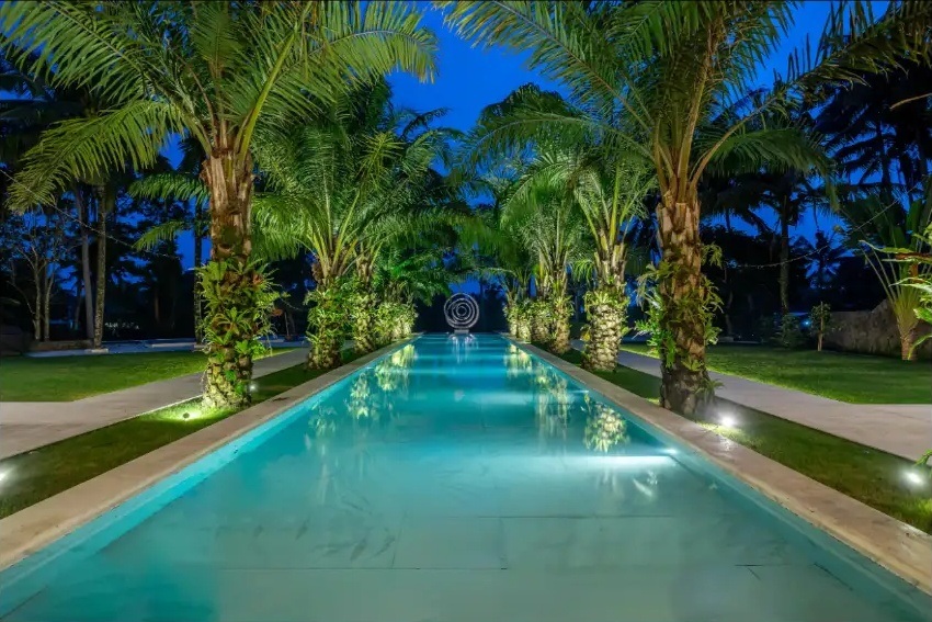 Palm-lined private villa swimming pool illuminated at dusk