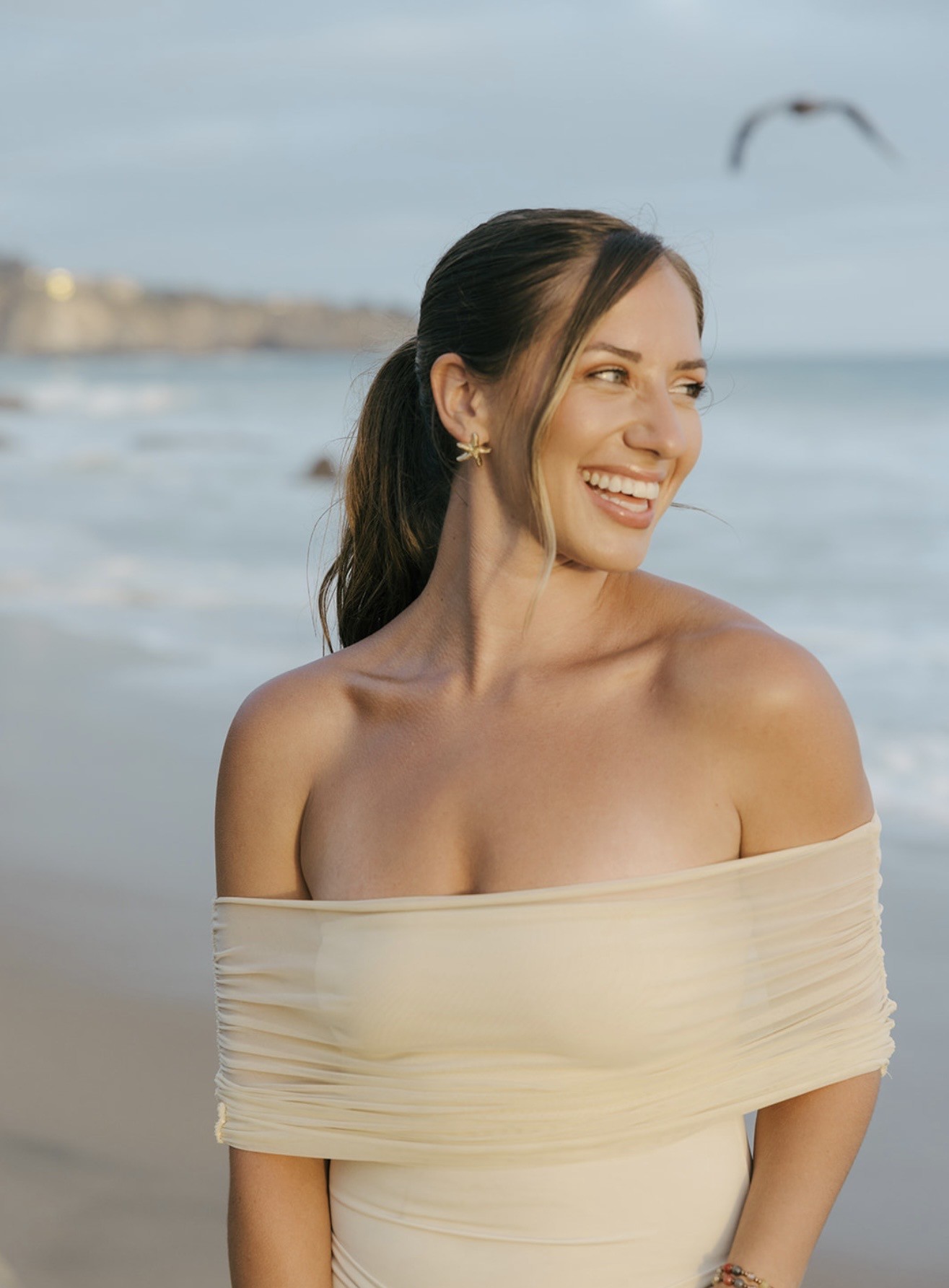 Rachel McElreath smiling on a beach in a cream off-the-shoulder dress