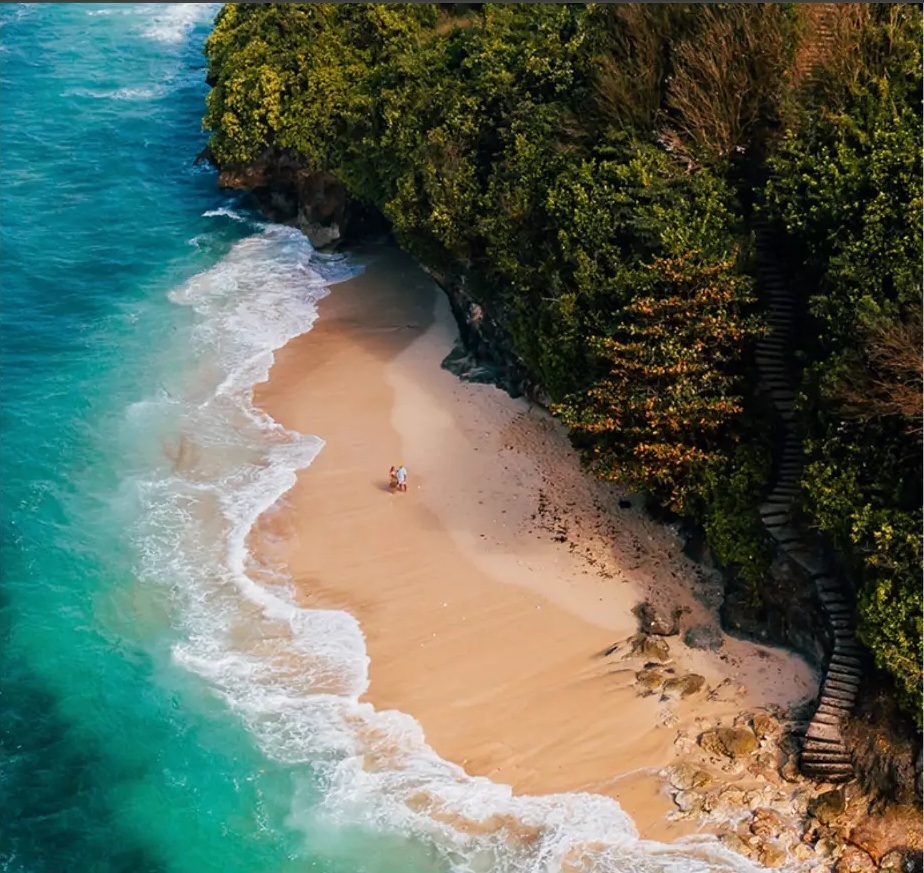 Turquoise ocean meeting a secluded Bali beach below green cliffs